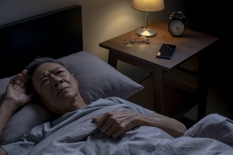 Senior man lays in bed in a nursing home facility.