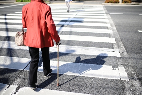 An elderly pedestrian crossing a crosswalk with a cane