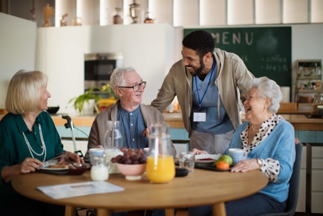 Nursing home residents eating and talking with aide